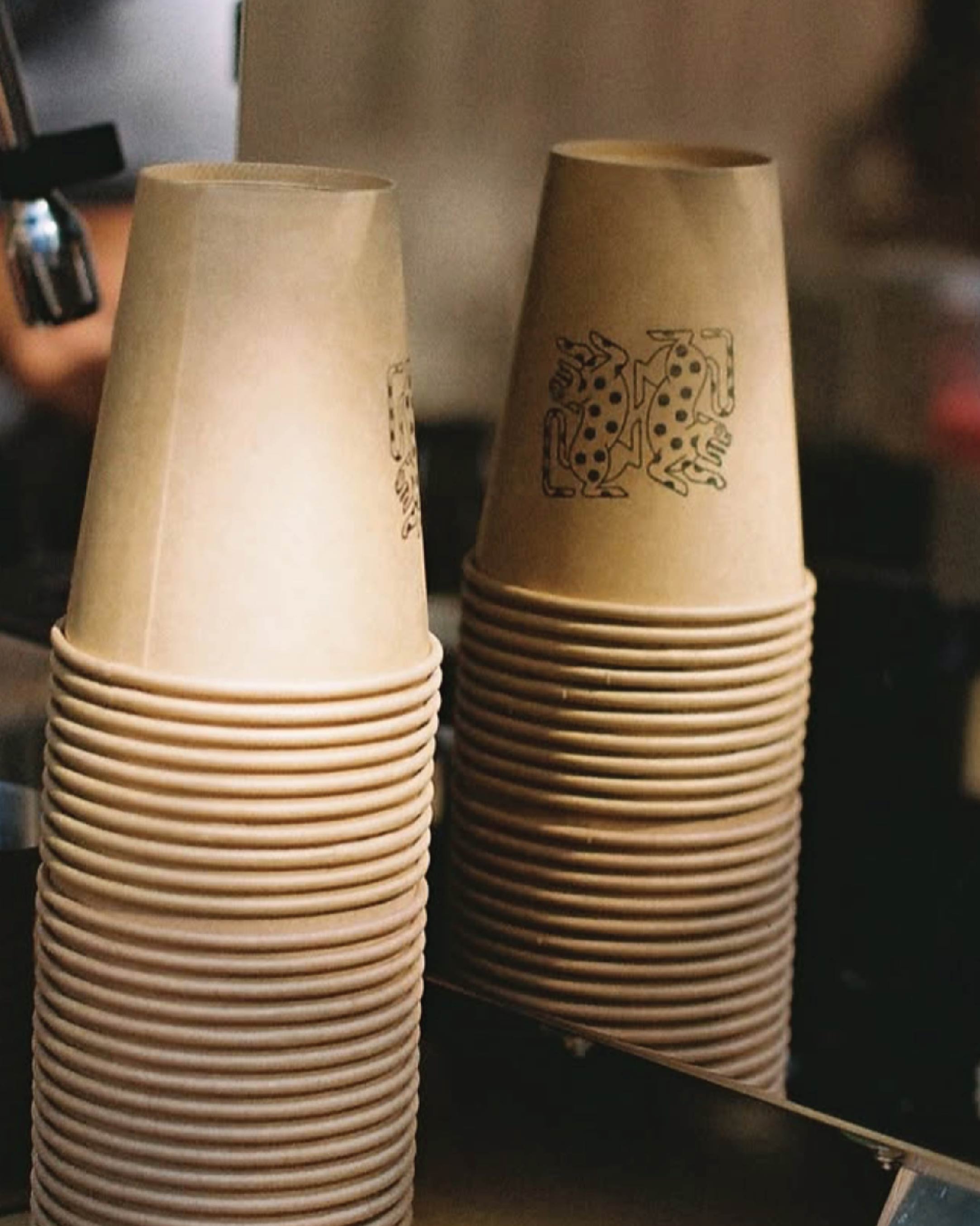 Alma Oscura — stacks of kraft paper cups printed with the jaguar mark, ready on the bar