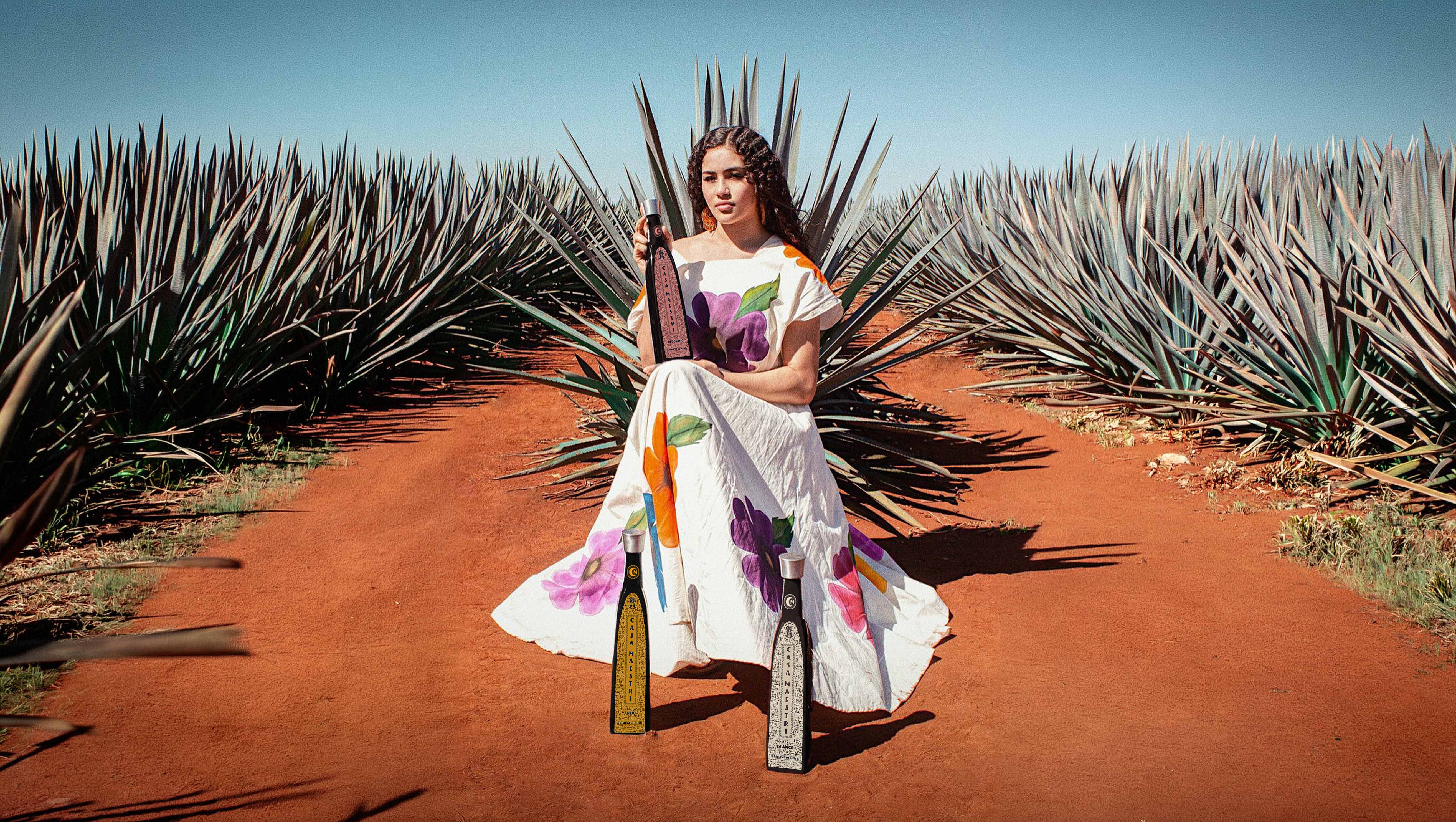 Casa Maestri — woman in a painted dress seated in an agave field with the Casa Maestri Reposado, Añejo and Blanco bottles