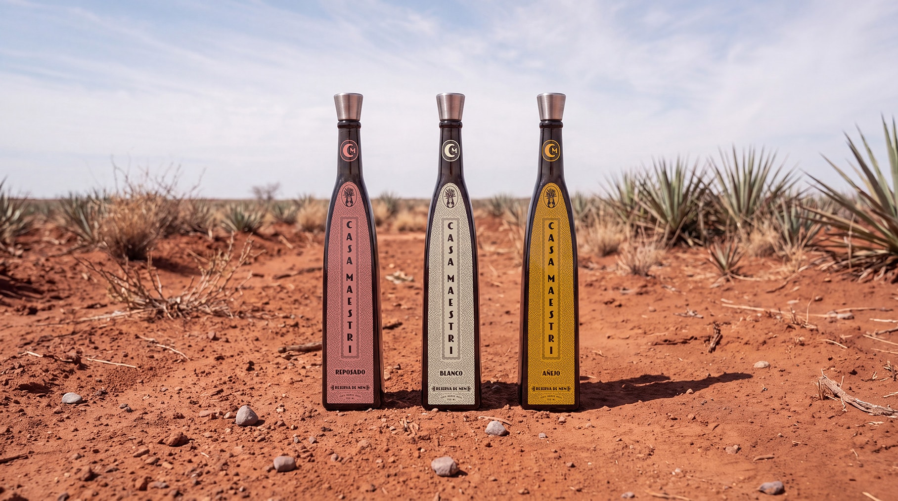 Casa Maestri — Reposado, Blanco and Añejo bottles standing in red soil in front of an agave field